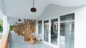 A covered outdoor seating area with a long table and chairs, a hanging light fixture, and a view through large glass doors. - sea shell resort (Gili Trawangan)