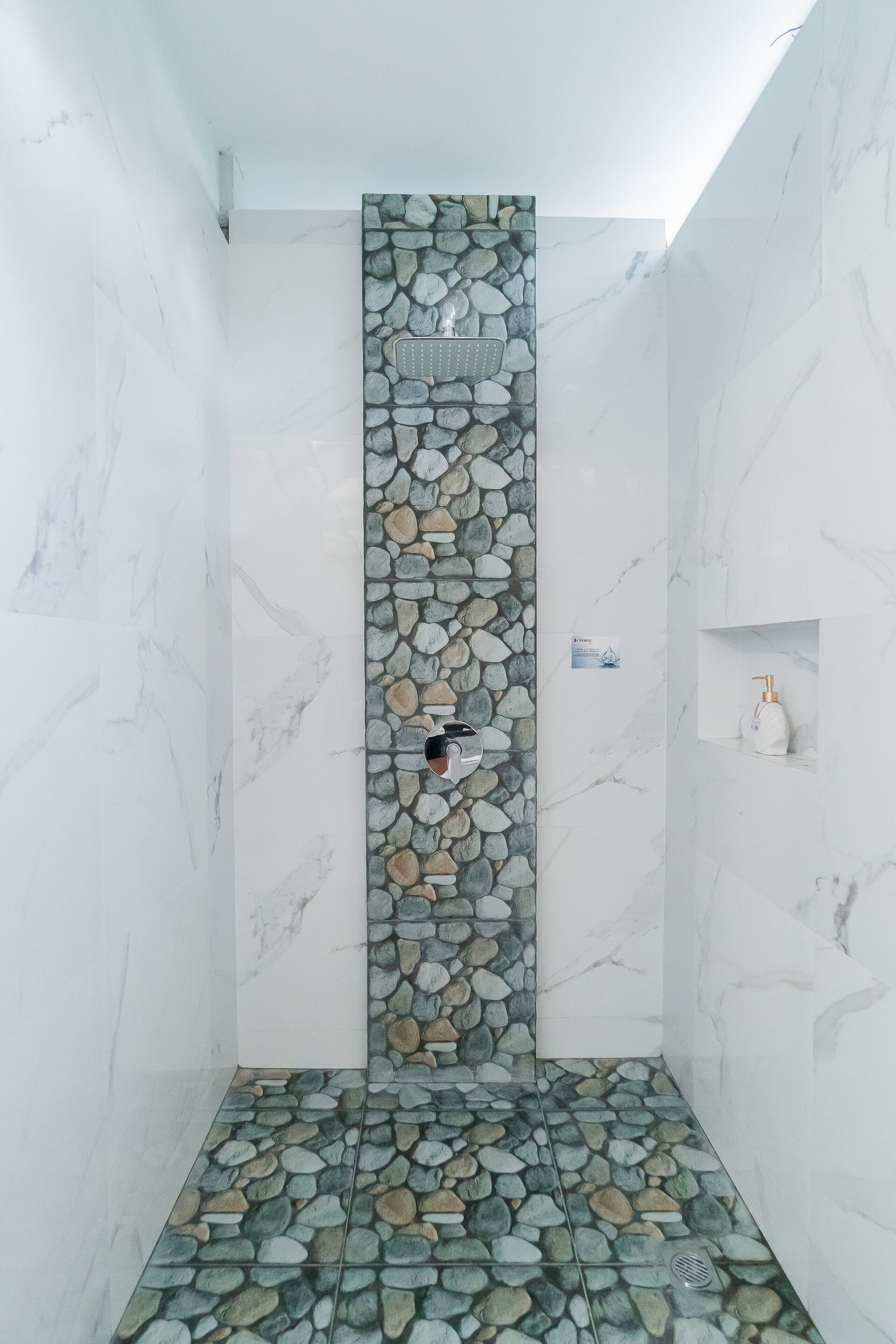 A shower area with a stone wall, a marble floor, and a small shelf with a bottle.