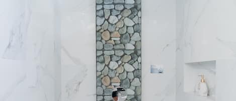 A shower area with a stone wall, a marble floor, and a small shelf with a bottle.