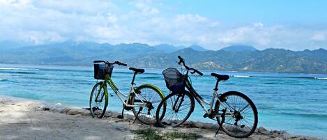 A bicycle parked on a sandy beach with a clear view of the ocean and mountains in the background.