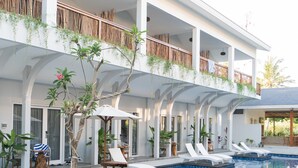 A poolside area with lounge chairs and a building with multiple balconies. - sea shell resort (Gili Trawangan)