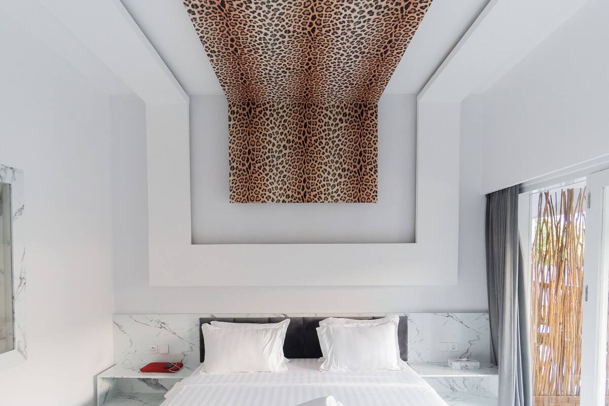 Une chambre à coucher moderne avec un grand lit, une tête de lit en marbre et une œuvre d’art originale à motif léopard peinte au plafond.