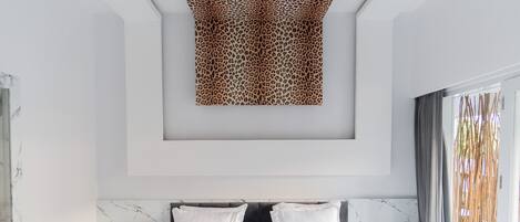 A modern bedroom with a large bed, marble headboard, and a unique leopard print artwork on the ceiling.