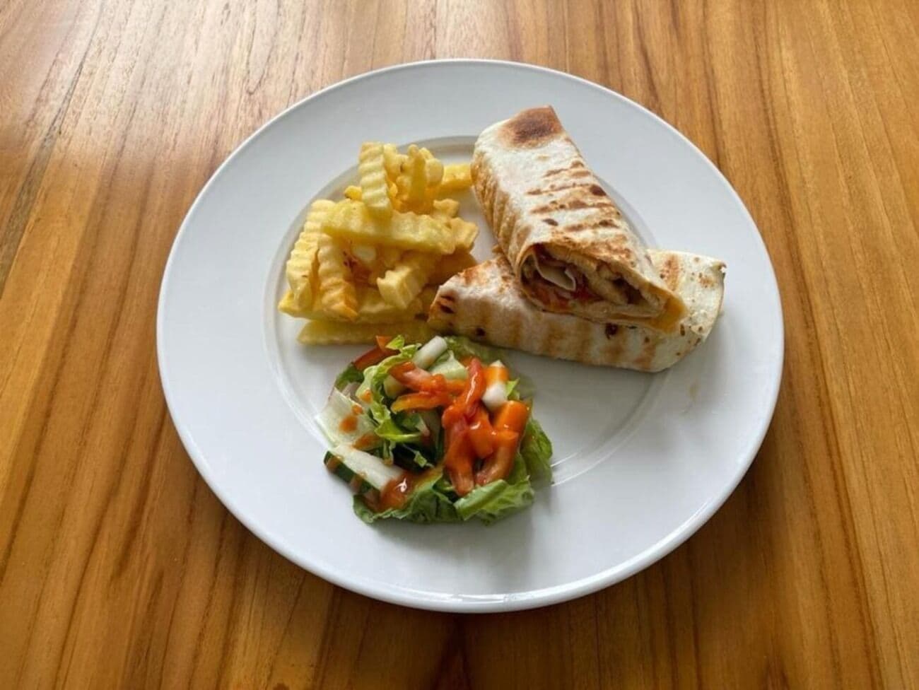 A plate with a wrap, fries, and a salad on a wooden table.