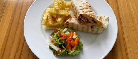 A plate with a wrap, fries, and a salad on a wooden table.
