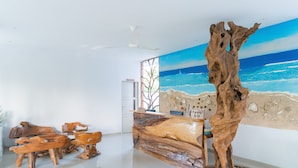 A room with a wooden reception desk and chairs, a large painting of a beach scene, and a ceiling fan. - sea shell resort (Gili Trawangan)