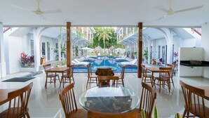 A spacious indoor area with a glass table surrounded by wooden chairs, a pool in the background, and a ceiling fan. - sea shell resort (Gili Trawangan)