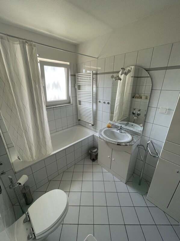 A bathroom with a bathtub, sink, toilet, and a window with a curtain.