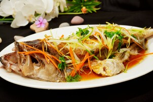 A plate of cooked fish with vegetables and sauce.