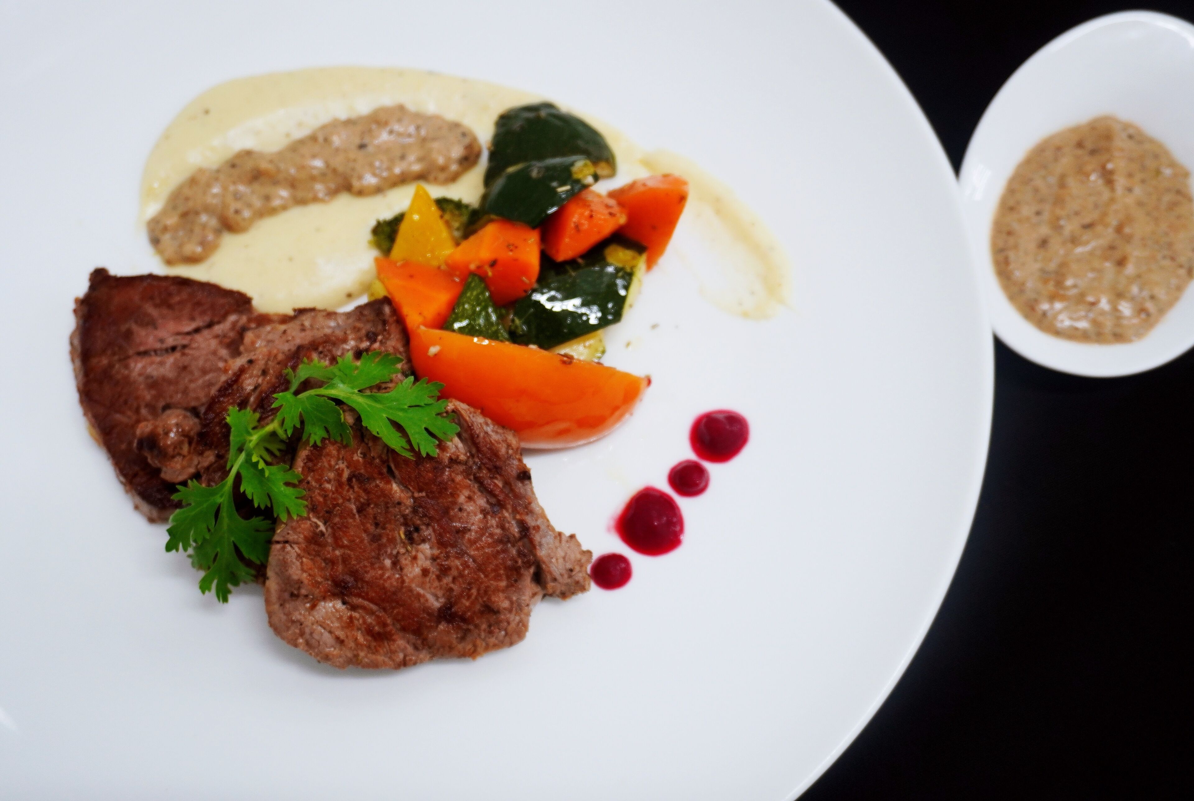 Un plato con un filete, verduras y salsa.