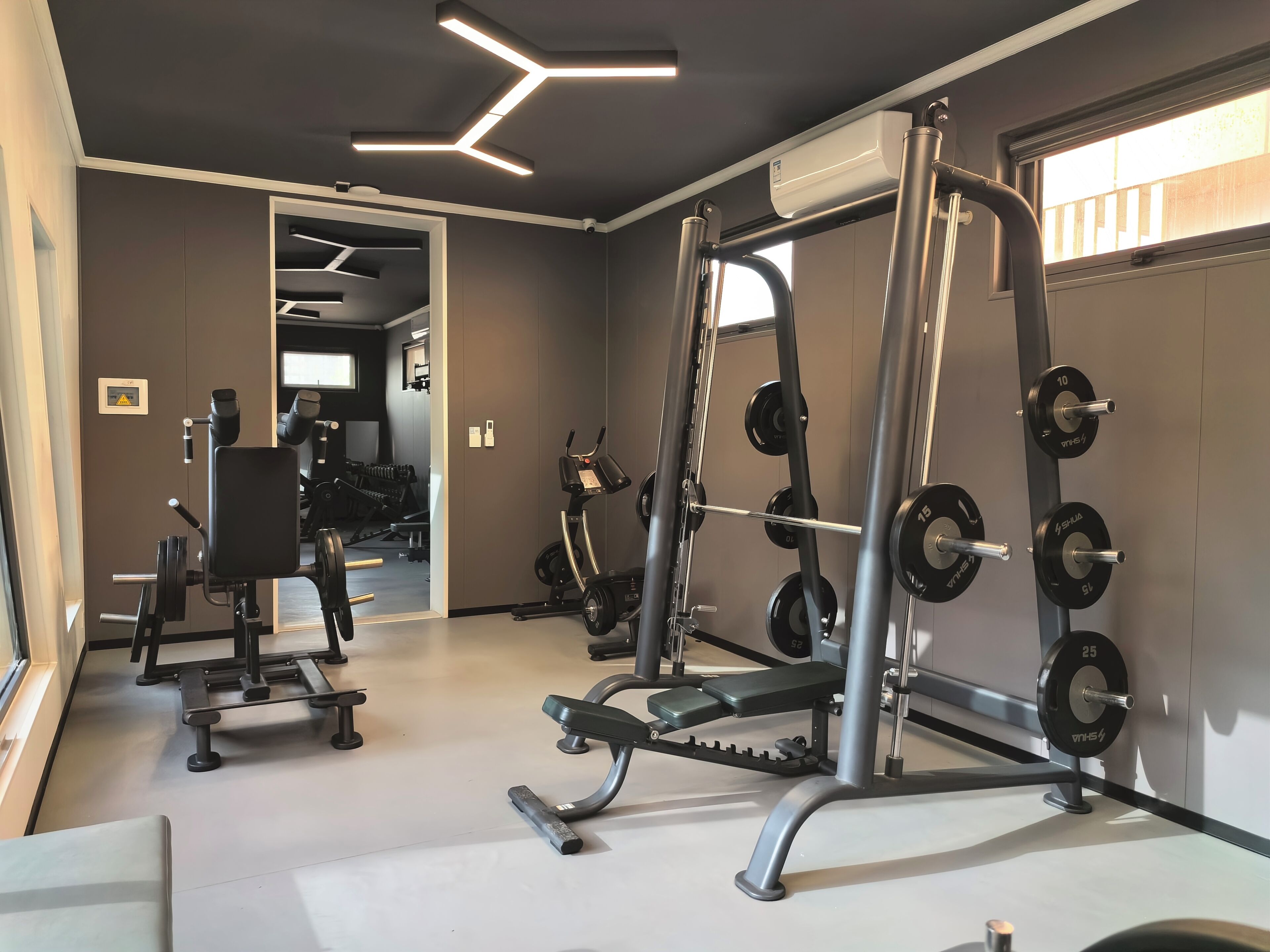 Een fitnessruimte met diverse trainingsapparaten, waaronder een squatrek, een bankdrukpers en dumbbells.