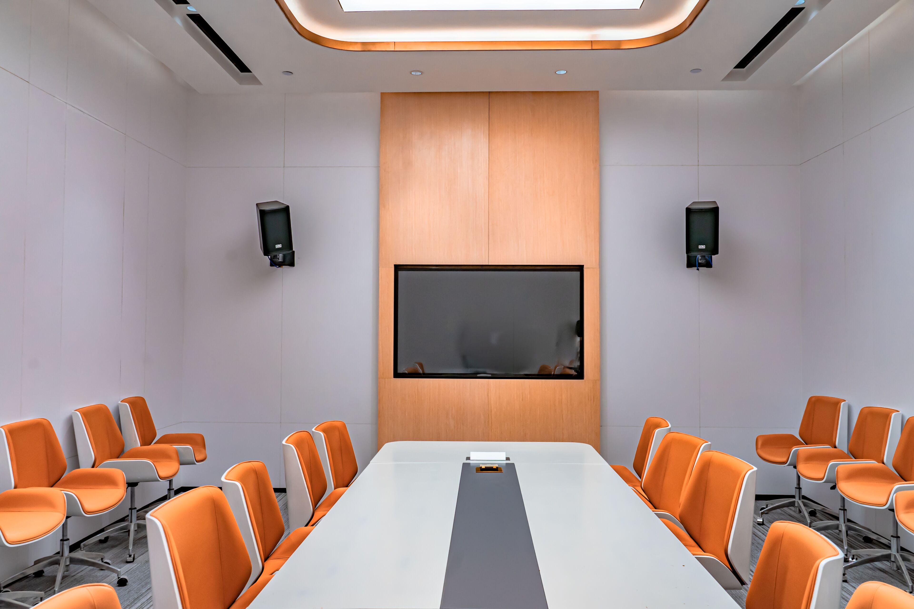 Un salón de conferencias con una larga mesa, sillas naranjas, una pantalla grande y dos oradores.