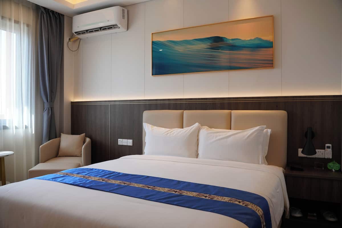 A hotel room with a large bed, a chair, a bedside table, and a painting on the wall.