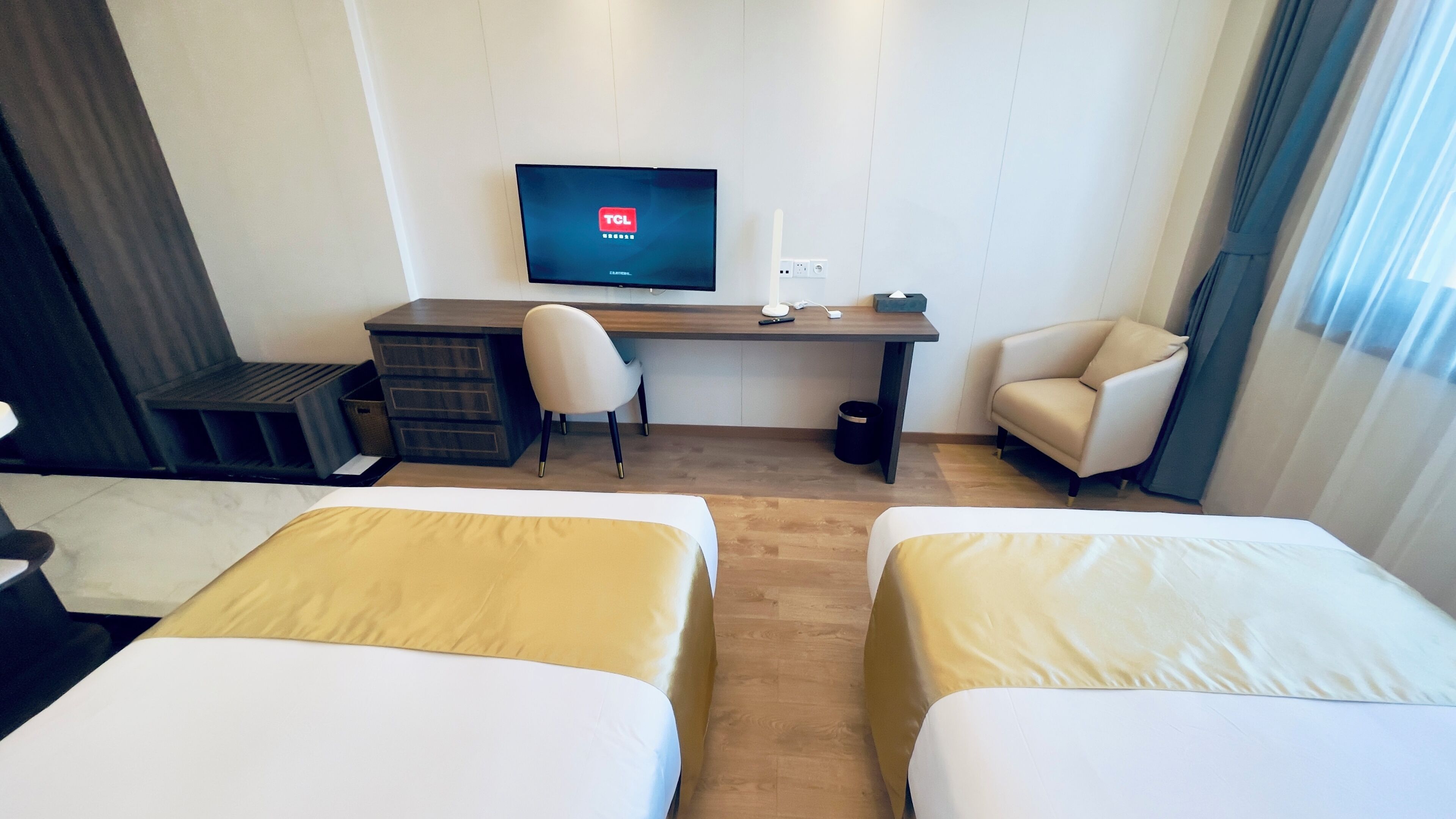 A hotel room with two beds, a desk with a TV, a chair, and a small table.