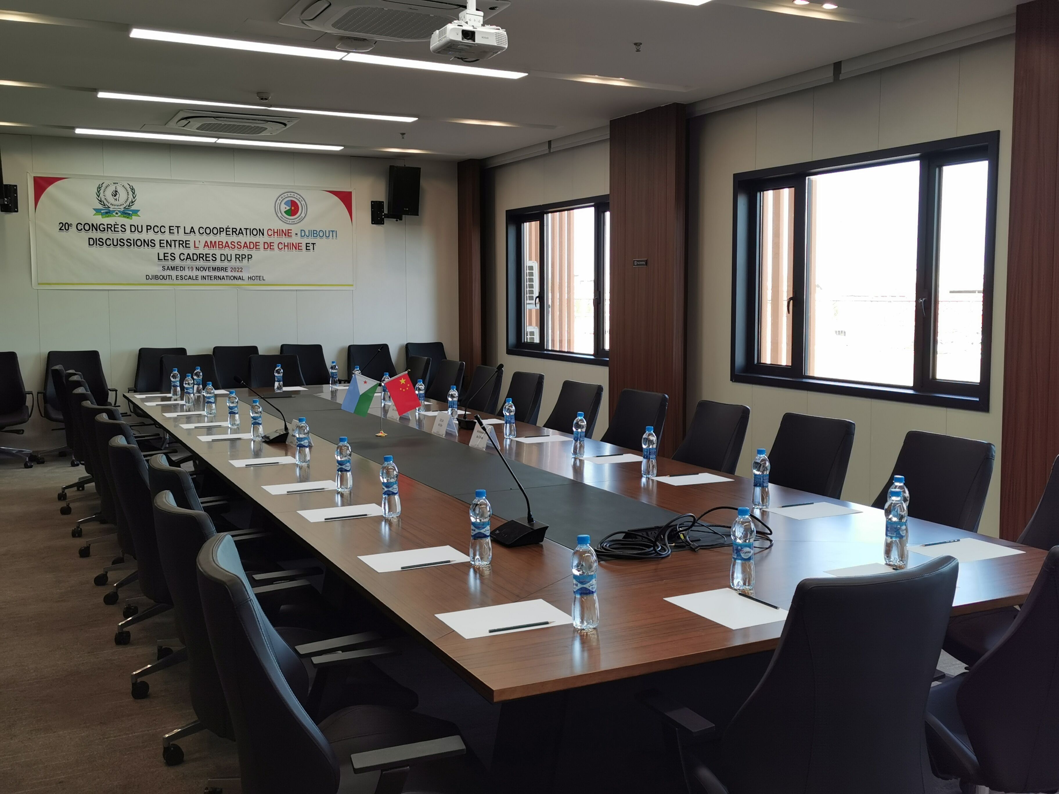 A conference room with a long table, chairs, water bottles, and flags.