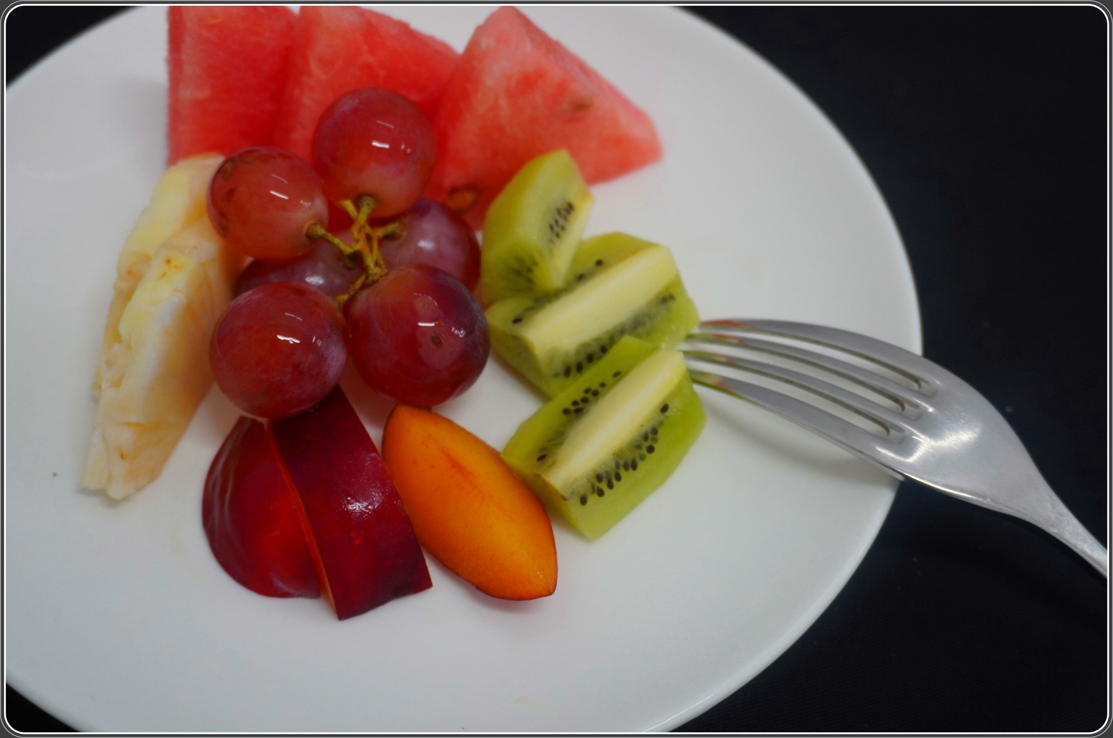 Un plato con varias frutas, incluyendo sandía, uvas, kiwi, melocotón y una naranja.