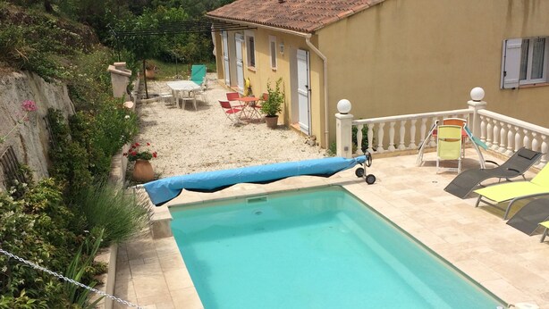 Une piscine rectangulaire avec une terrasse carrelée, entourée d’une clôture blanche et surmontée d’un auvent bleu.