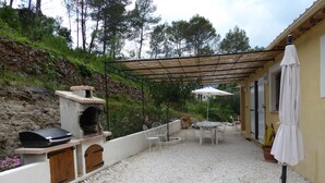 Une terrasse extérieure équipée d’un barbecue, d’une pergola, de meubles de jardin et de plantes en pot.