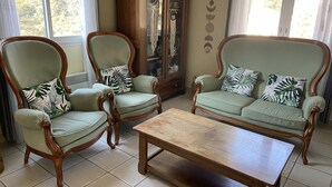Une pièce comprenant deux fauteuils verts, recouverts d’un tissu d’ameublement et dotés d’une structure en bois, ainsi que des coussins assortis, une table basse en bois et un buffet en bois avec des portes en verre.