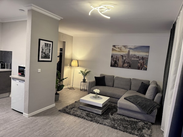 Uma sala de estar moderna com um sofá cinza, uma mesa de centro, um abajur e uma pintura com vista para a cidade na parede.