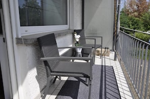 Varanda com cadeira, mesa e um pequeno vaso de planta, além de vista para o verde.
