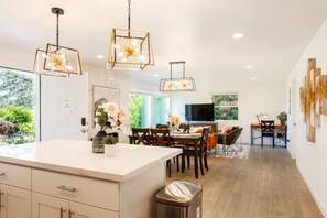 A modern kitchen with a large island, dining area, and a TV in the background. - 6615 Lower · 3b2b Lower Unit w/ Gorgeous Green Lake View (Seattle)