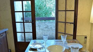 Een eetgedeelte met een tafel voor twee personen, uitzicht op groen en een deur met een raam.
