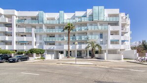 A multi-story hotel with balconies, a palm tree in the foreground, and a clear blue sky.