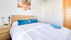 A bedroom with a bed, a nightstand, a lamp, a wall-mounted picture, and a wardrobe.