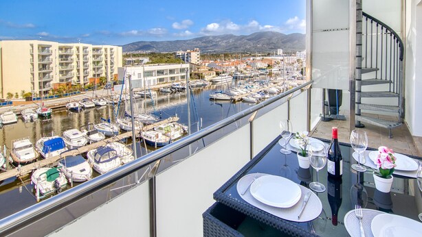 A balcony with a table set for dining, overlooking a marina with boats and buildings.
