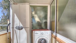 A compact laundry area with a washing machine, a drying rack, and a hose. - CANT DELS OCELLS 19 Roses (Rosas / Roses)