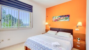 A bedroom with a bed, two bedside lamps, a painting on the wall, and a window with blinds. - CANT DELS OCELLS 19 Roses (Rosas / Roses)