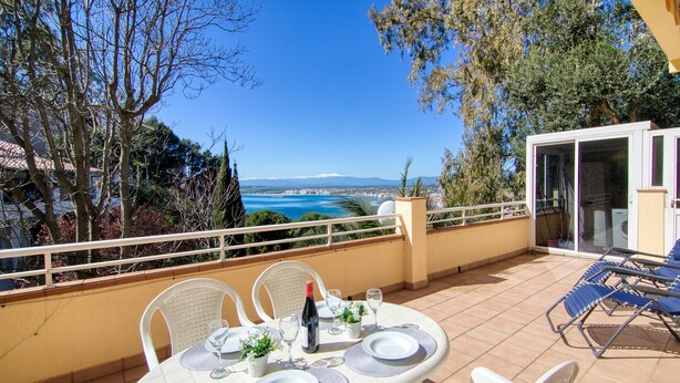 A terrace with a table set for two, overlooking a scenic view of the sea and mountains. - CANT DELS OCELLS 19 Roses (Rosas / Roses)