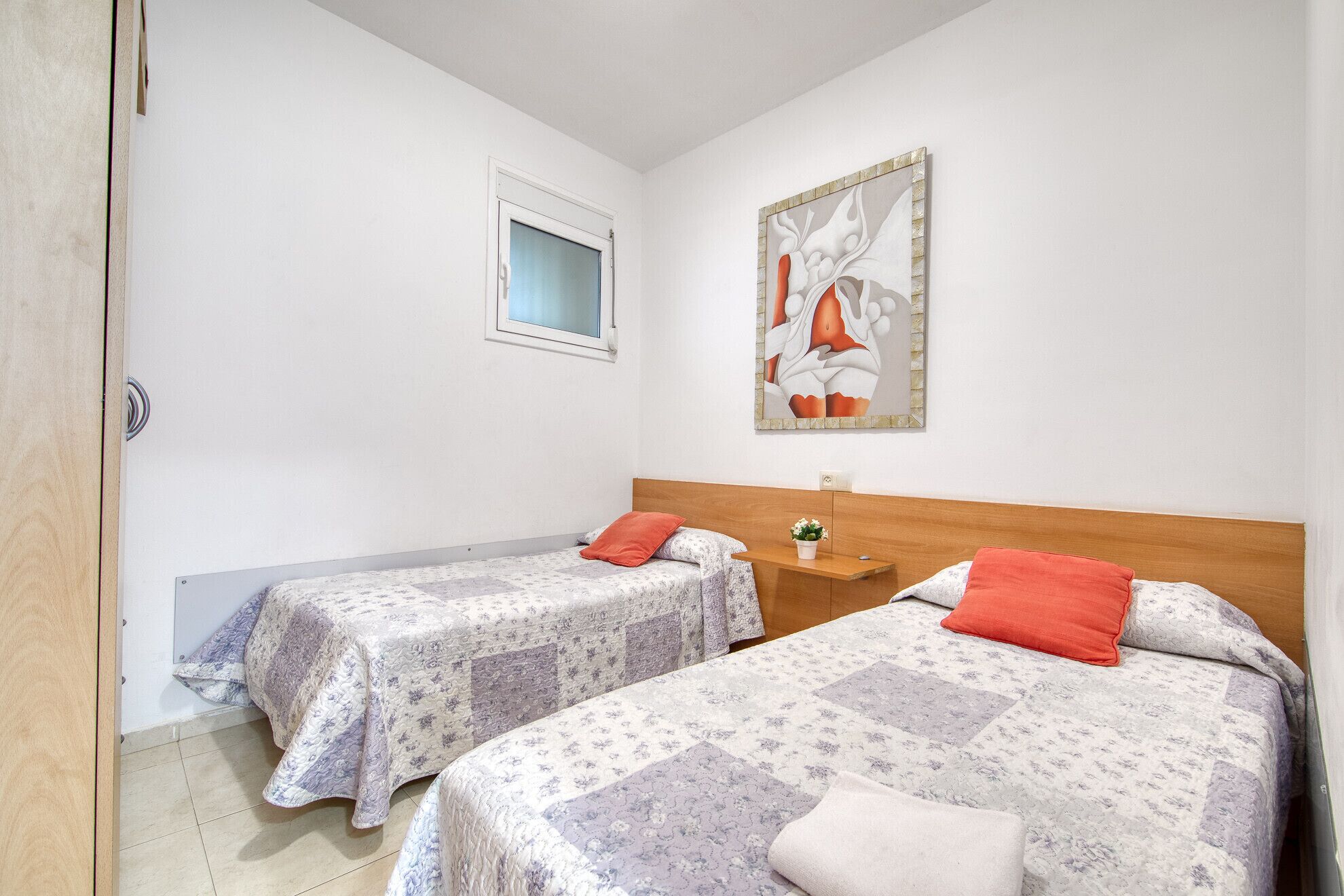 A room with two beds, a window, and a painting on the wall.