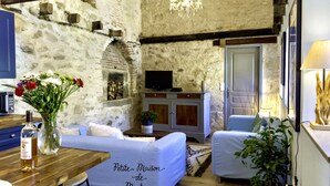 A cozy room with a stone wall, a wooden table with a bottle, a white sofa, and a television on a cabinet. - Renovated barn,  great for countryside walks, and bike rides (Azat-le-Ris)