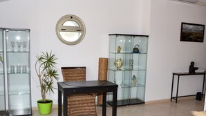 A modern living room with a dining table, chairs, a potted plant, glass display cabinets, and a small table with decorative items.