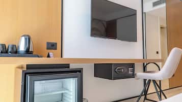 A compact room with a flat-screen TV mounted on the wall, a small refrigerator, a chair, and a coffee maker on the counter.