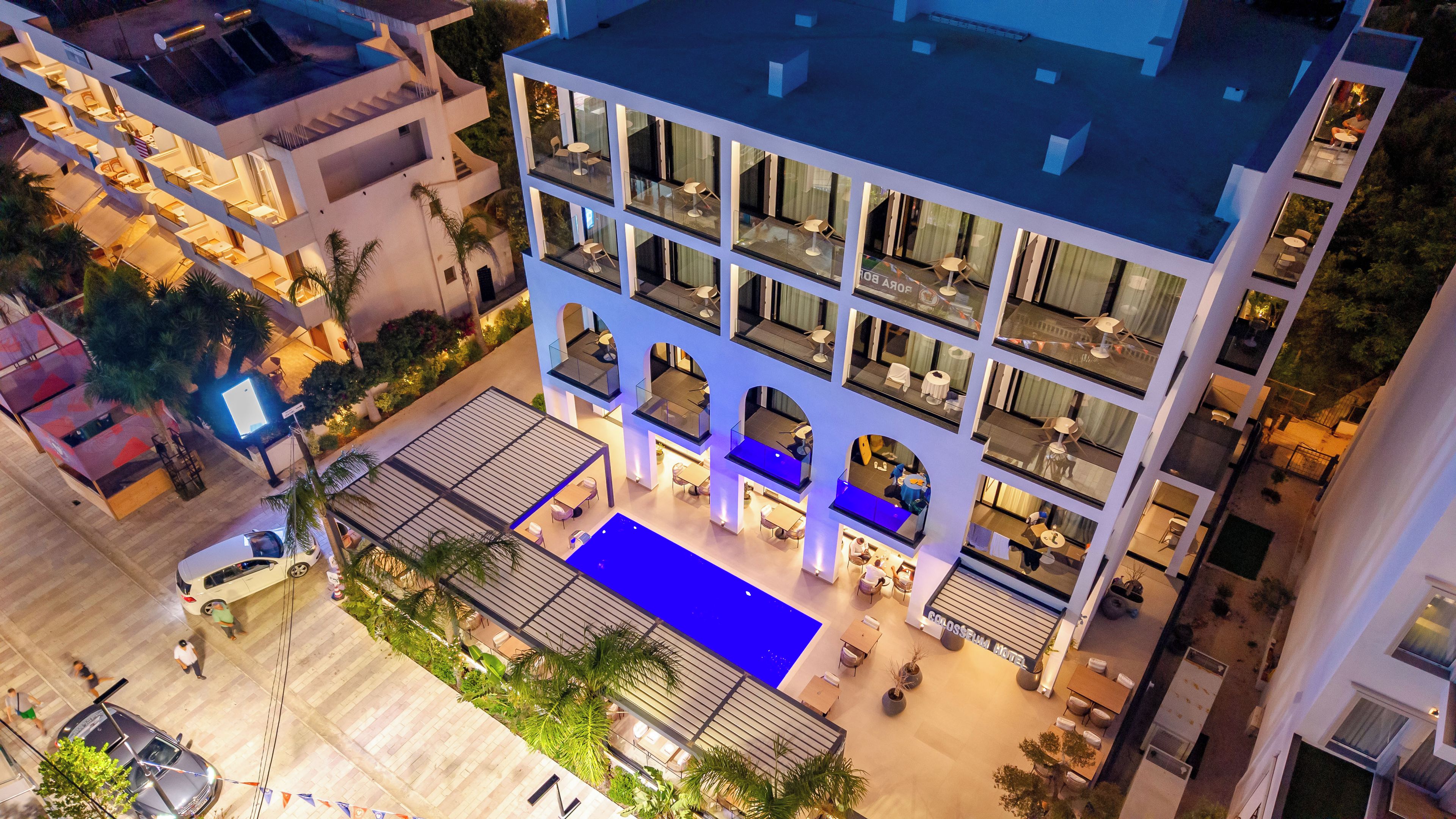 Un hotel de varios pisos con piscina en la azotea, zona de estar exterior y fachada bien iluminada.