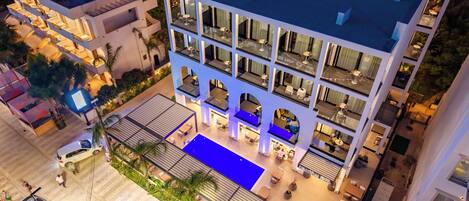 A multi-story hotel with a rooftop pool, outdoor seating, and a well-lit facade.