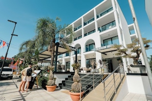 A modern hotel with a glass facade, outdoor seating, and a staircase leading to the entrance. - Hotel Colosseum (Ksamil)