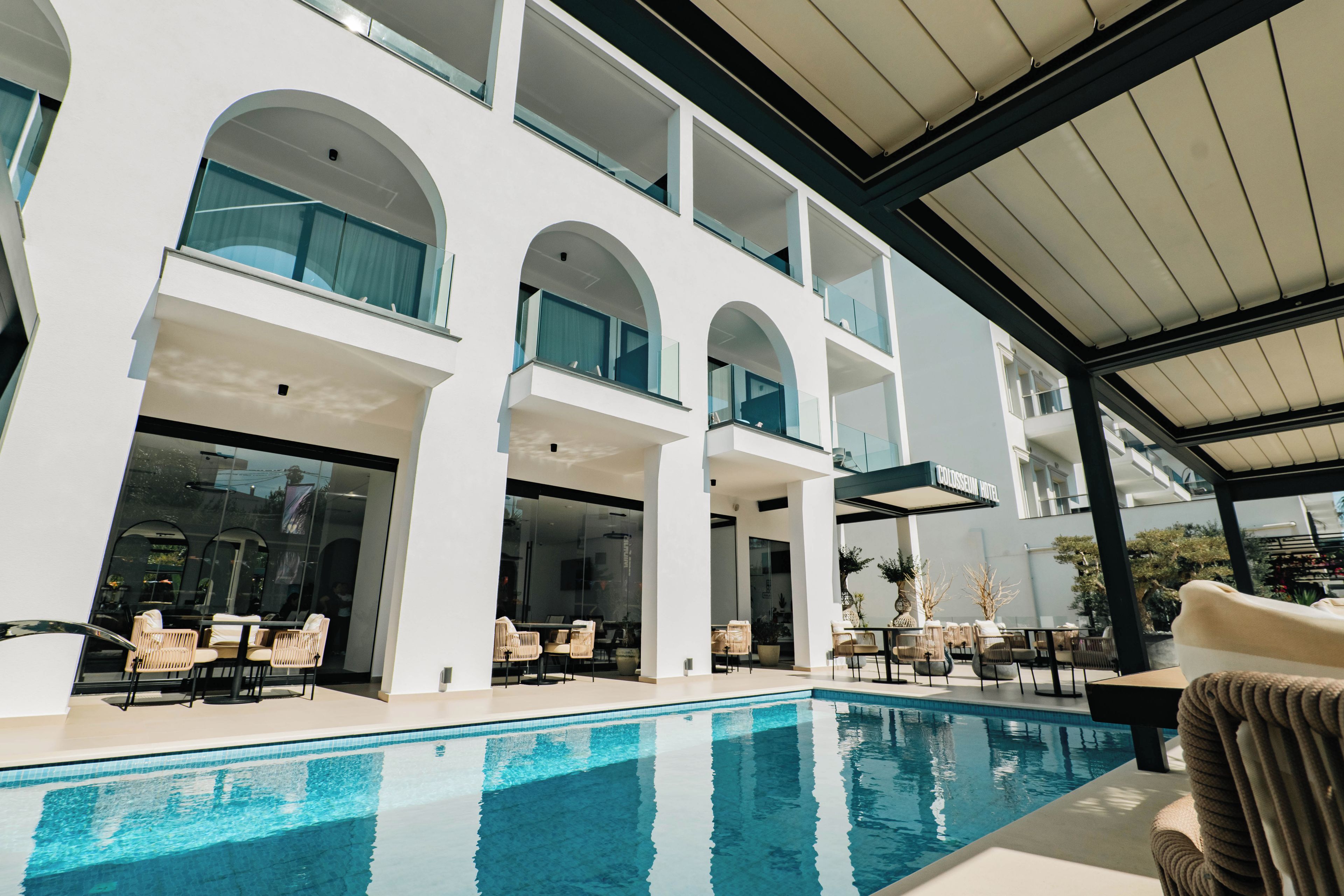 A modern hotel with a pool area, outdoor seating, and a covered patio.
