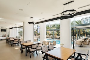 A modern indoor dining area with tables and chairs, large windows, and a view of an outdoor pool area.
