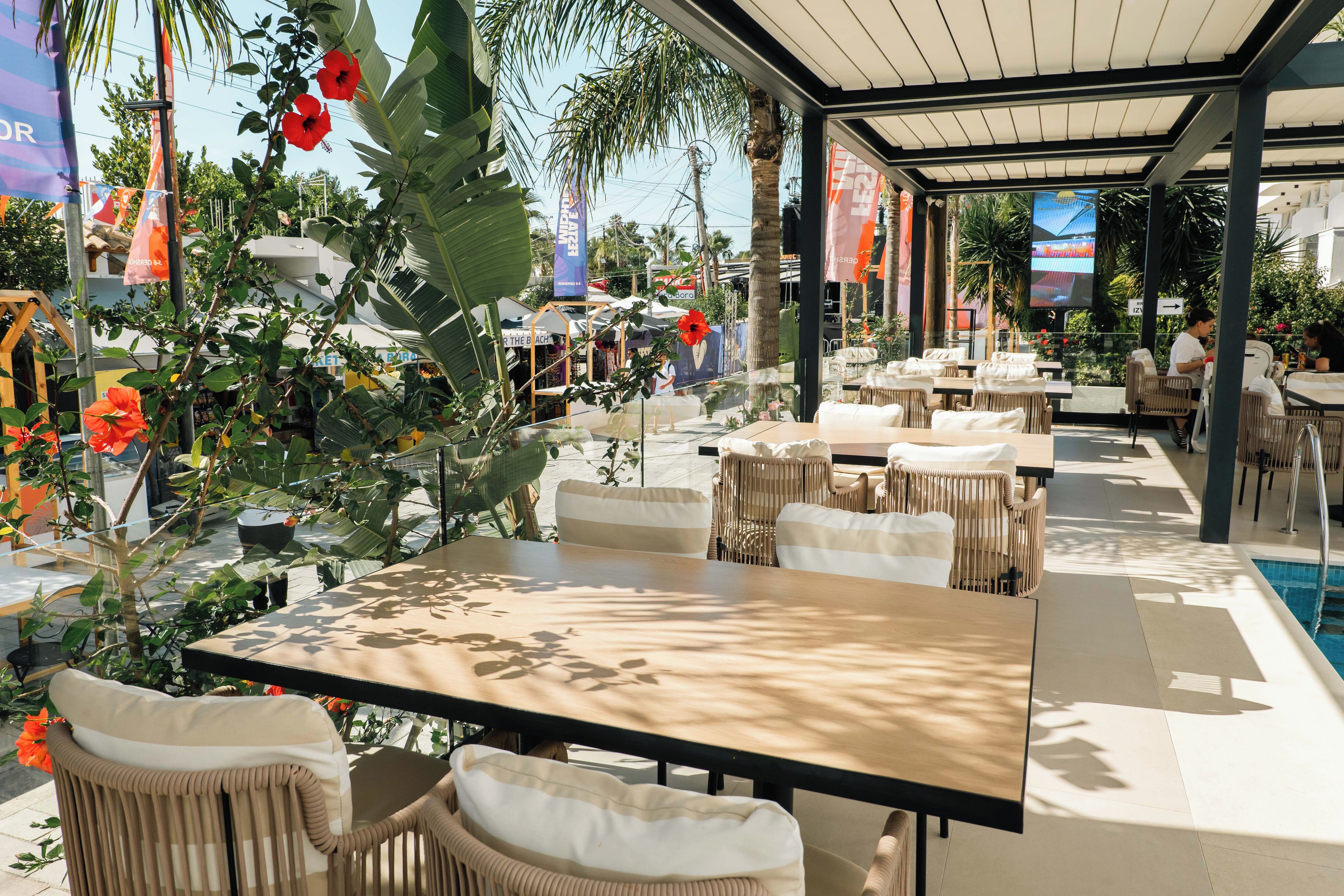 Un espace extérieur aménagé avec des tables et des chaises, entouré de plantes et de fleurs tropicales.