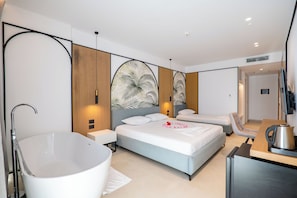 A modern hotel room with a large bathtub, two beds, a seating area, and a flat-screen TV. - Hotel Colosseum (Ksamil)