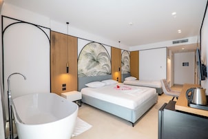 A modern hotel room with a large bathtub, two beds, a seating area, and a flat-screen TV.