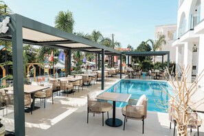 An outdoor pool area with lounge chairs and tables, surrounded by a covered seating area and a pool. - Hotel Colosseum (Ksamil)