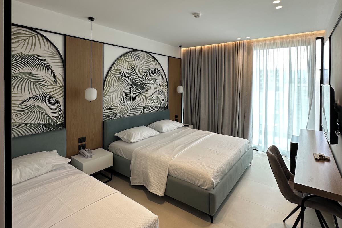 A modern hotel room with two beds, a desk, and a large window with curtains.