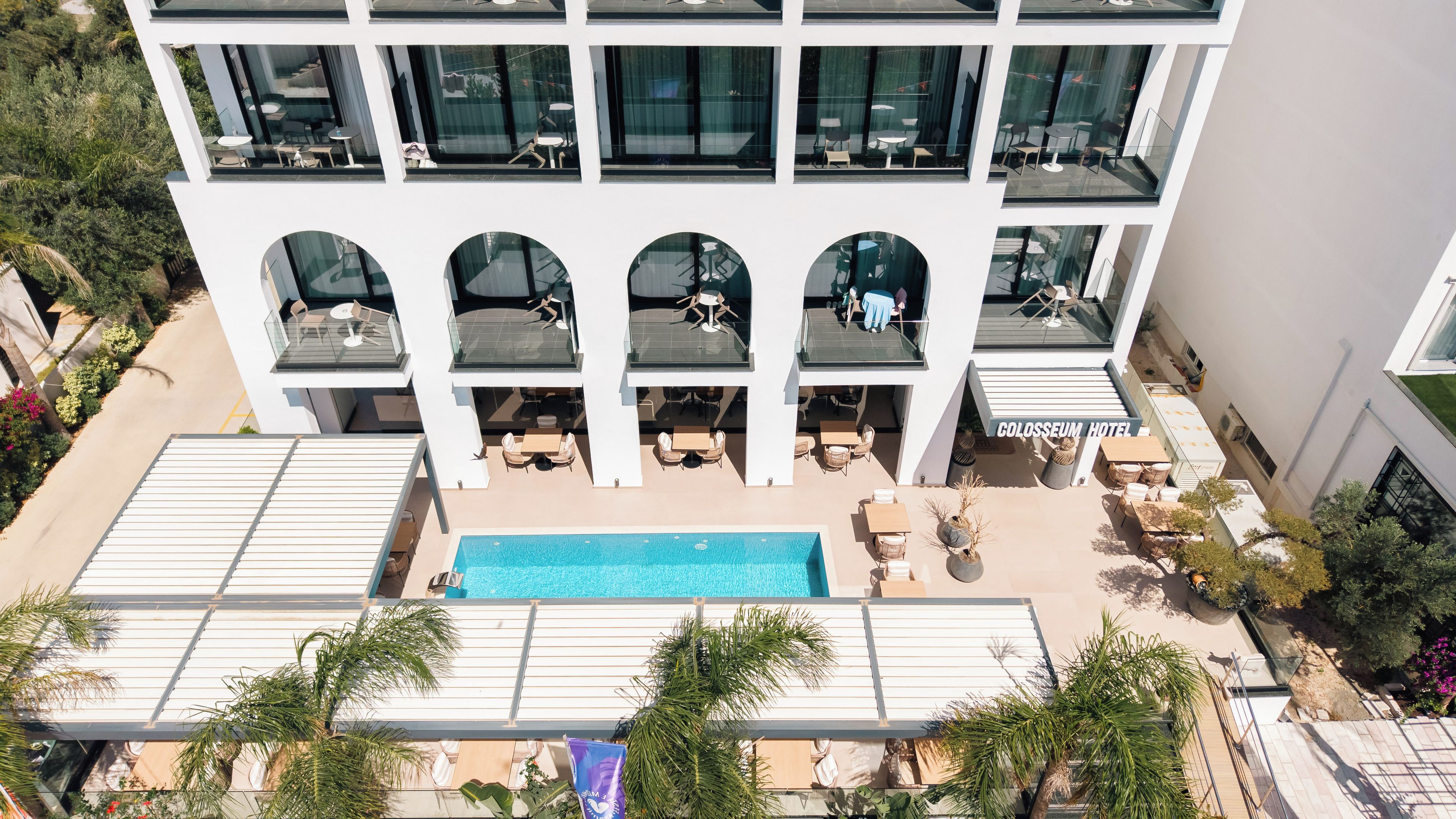 Un hotel moderno con varios balcones, piscina y zonas de estar al aire libre.
