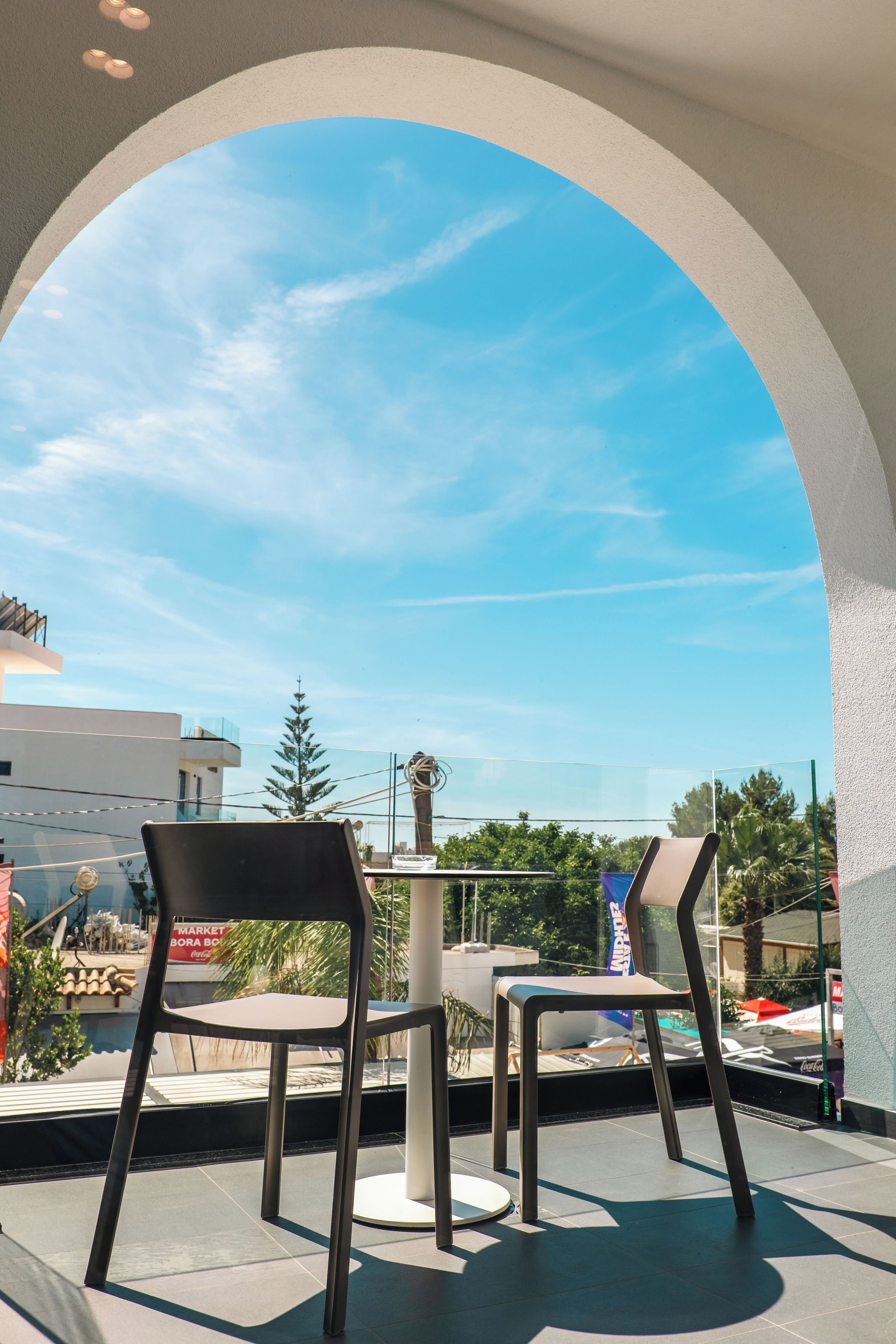 Una terraza con dos sillas y una mesa, con vistas a un cielo despejado y edificios y árboles.