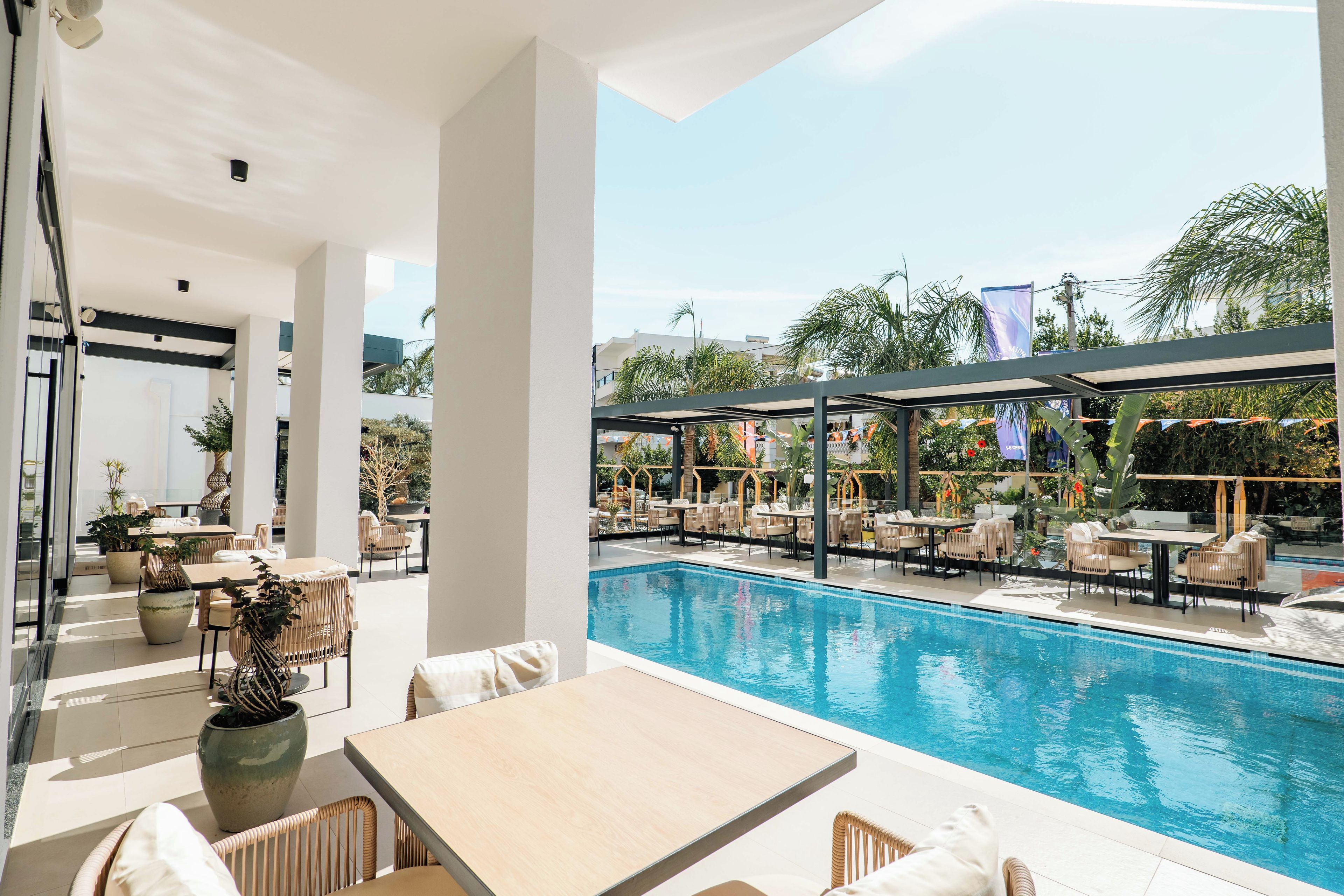 A poolside area with tables and chairs, a clear view of the pool, and a covered seating area with umbrellas.